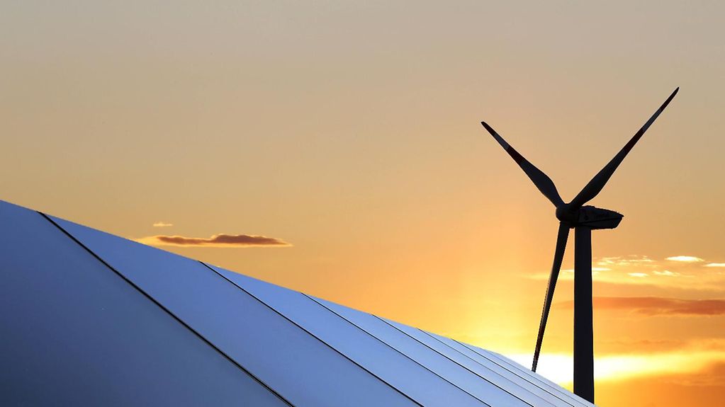 Solar panels and a wind turbine in front of a sunset panorama.
