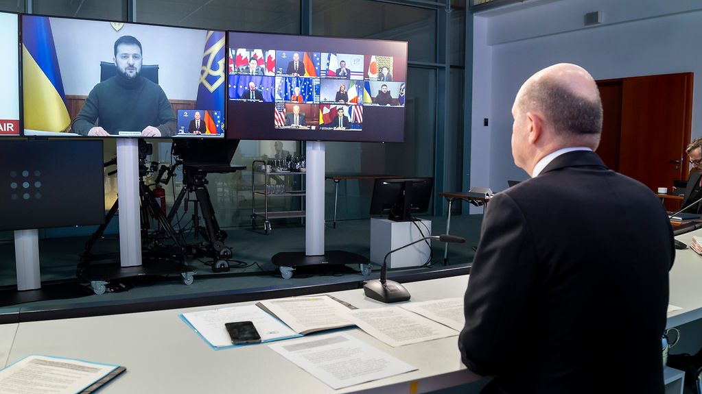 The photo shows Federal Chancellor Scholz facing a screen which shows Ukraine's President Zelensky speaking.