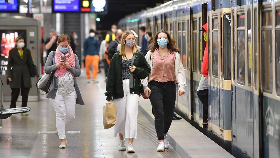 Auf dem Foto sind Bahnreisende mit Maske neben einem Zug zu sehen.