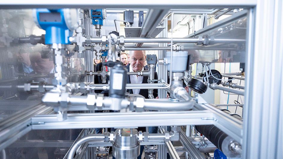 Bundeskanzler Scholz blickt durch eine Anlage im Zentrum für Brennstoffzellentechnik in Duisburg