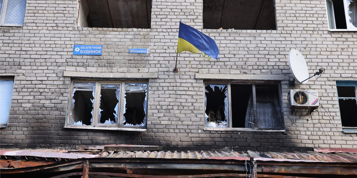 Eine ukrainische Flagge weht an der Außenwand eines vom Krieg zerstörten Hauses in der Ukraine.