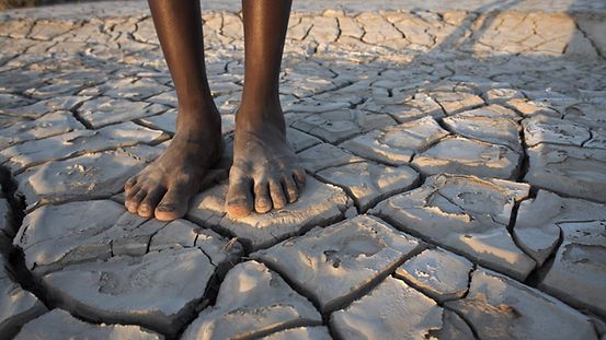 Foto zeigt eine Person in Afrika auf ausgetrocknetem Boden. 