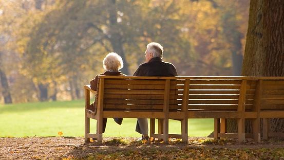 Un couple de personnes âgées est assis sur un banc public à l’automne.